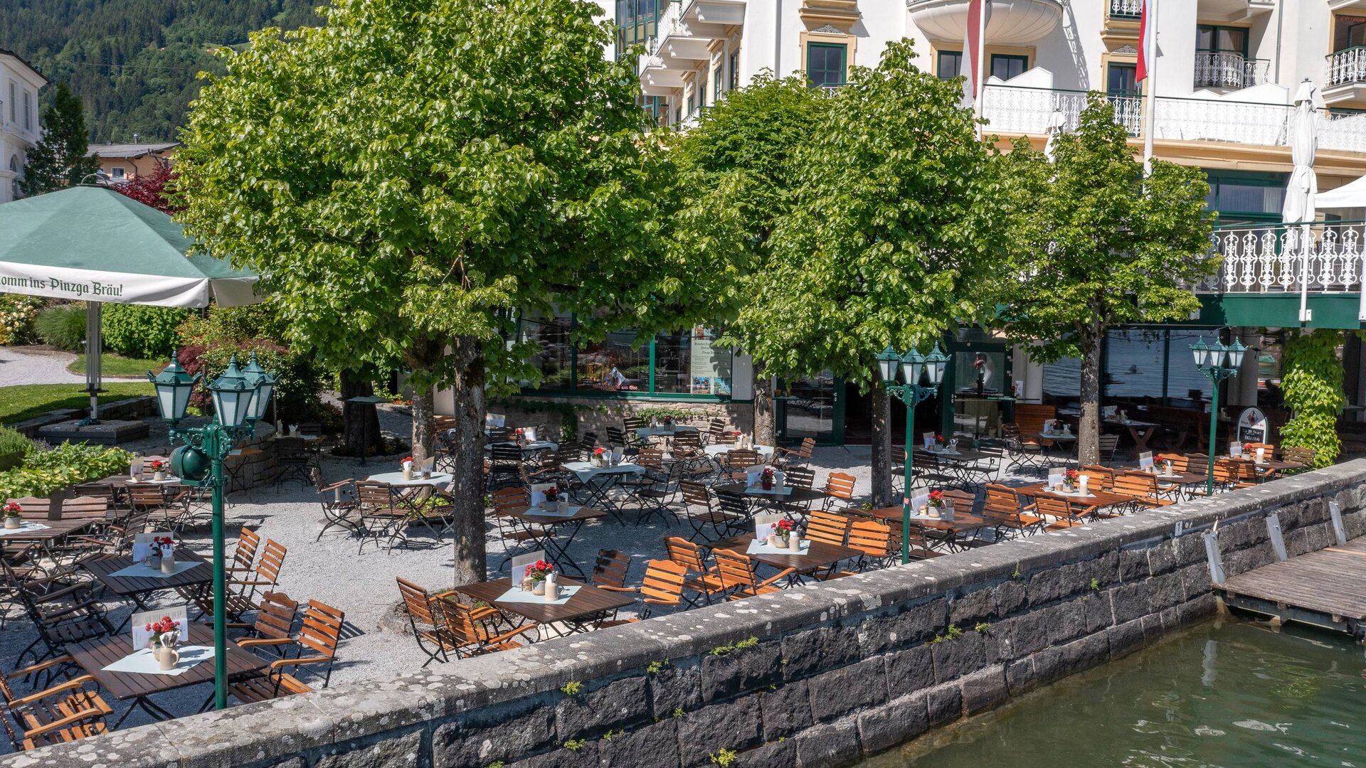 Der Gastgarten des Pinzga Bräu liegt direkt am Zeller See mit Tischen, Stühlen, Sonnenschirmen und Blick auf das Ufer.