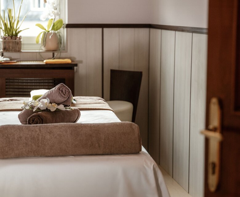 Ein Behandlungsbett im Wellnessraum mit Handtüchern und dekorativem Pflanzenarrangement.