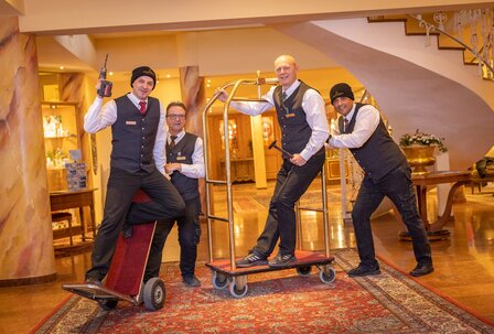 Hotelpersonal mit Gepäckwagen im GRAND HOTEL Zell am See Vier Mitarbeiter in Hoteluniform stehen im Eingangsbereich mit Gepäckwagen und Werkzeugen.