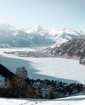 Der zugefrorene Zeller See liegt vor schneebedeckten Bergen und einer winterlichen Uferlandschaft.