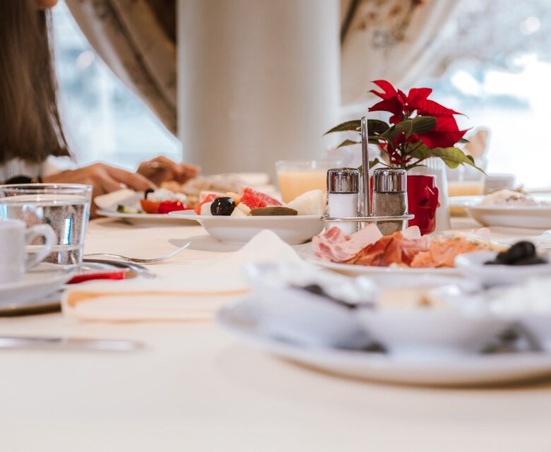 Ein gedeckter Frühstückstisch mit Gebäck, Obst, Aufschnitt und Getränken im Hotelrestaurant.