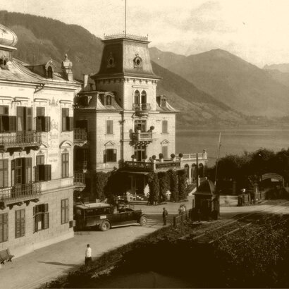 Historic hotel building by Lake Zell with towers, balconies, and mountains in the background.
