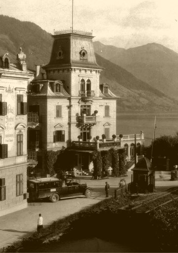 Historisches Hotelgebäude am Zeller See mit Türmen, Balkonen und Blick auf die Berge.