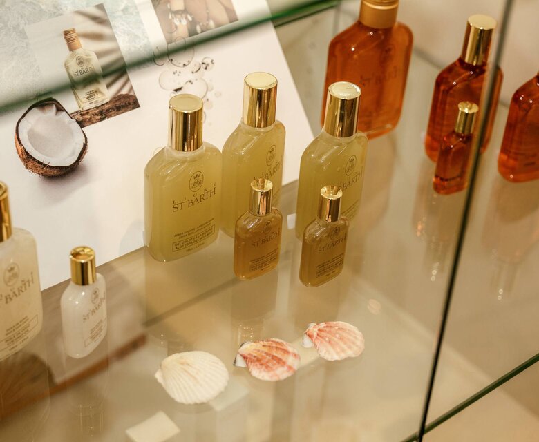 توجد عدة منتجات عناية بالجسم وزجاجات صغيرة مرتبة داخل خزانة عرض زجاجية.