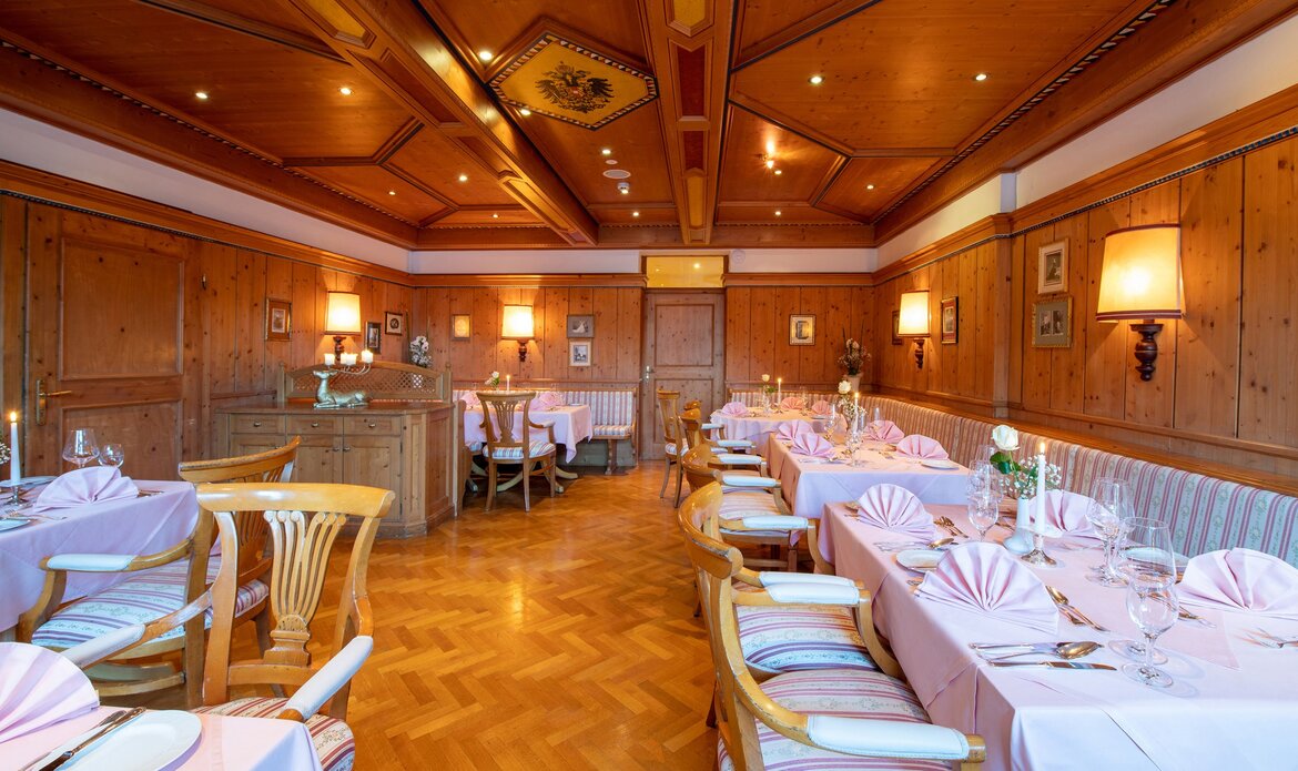 A wood-paneled dining room with set tables and warm lighting inside Restaurant Belvedere at GRAND HOTEL Zell am See.