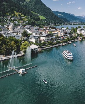 Ein Ausflugsschiff fährt über den Zeller See, im Hintergrund liegt der Ort Zell am See am grünen Berghang.