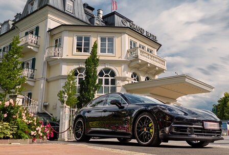 Luxusauto vor dem Grand Hotel Ein schwarzes Luxusauto steht vor dem Eingang des Grand Hotel mit heller Fassade und überdachtem Vorfahrtbereich.