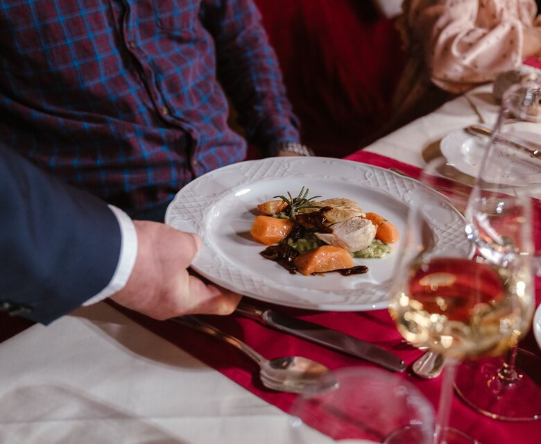 Ein Kellner reicht einem Gast im Hotelrestaurant einen Teller mit einem sorgfältig angerichteten Hauptgang.
