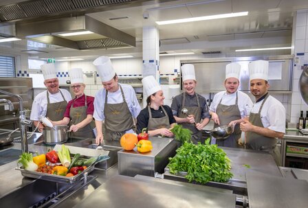 Küchenteam im GRAND HOTEL Zell am See Das Küchenteam steht in der Großküche und bereitet gemeinsam die Arbeit an den Edelstahlarbeitsflächen vor.