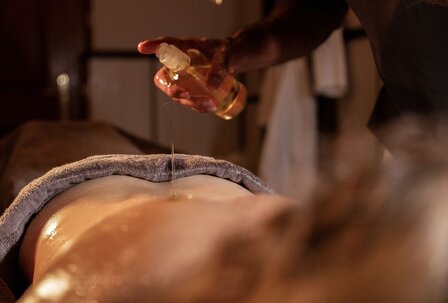 Wellnessbehandlung mit Öl im GRANDSPA Zell am See Eine Person gießt Öl auf den Rücken einer liegenden Person bei einer Wellnessbehandlung im Spa.
