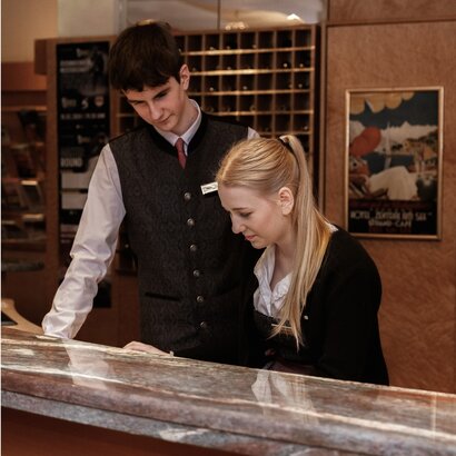 A female and male staff member stand at the reception desk and look down at the counter together.