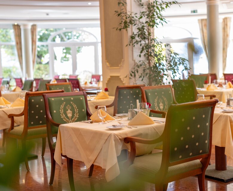Ein elegant gedeckter Speisesaal mit grün bezogenen Stühlen, eingedeckten Tischen und hellem Tageslicht.