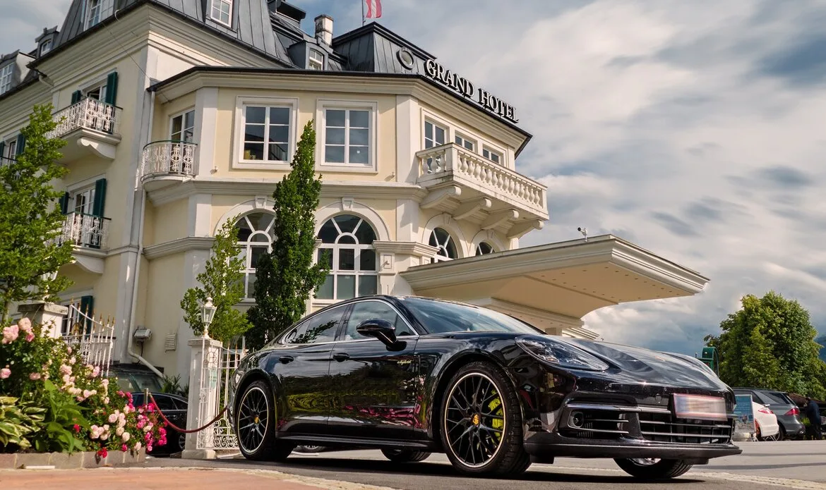 Ein schwarzer Sportwagen steht vor dem GRAND HOTEL Zell am See unter einem hellen Himmel.