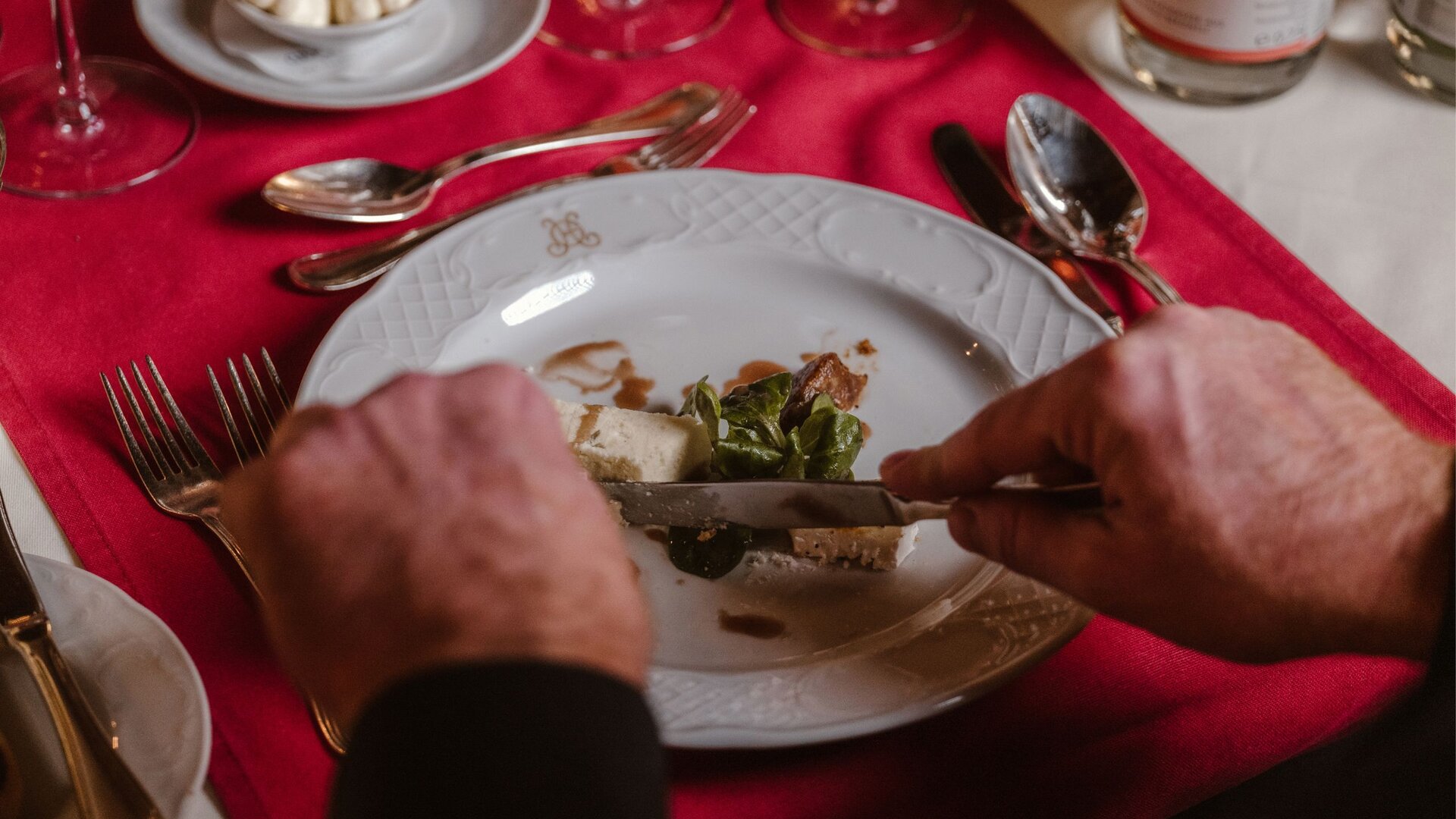 Eine Person schneidet im Hotelrestaurant ein angerichtetes Abendessen mit Fleisch, Gemüse und Sauce auf weißem Teller.