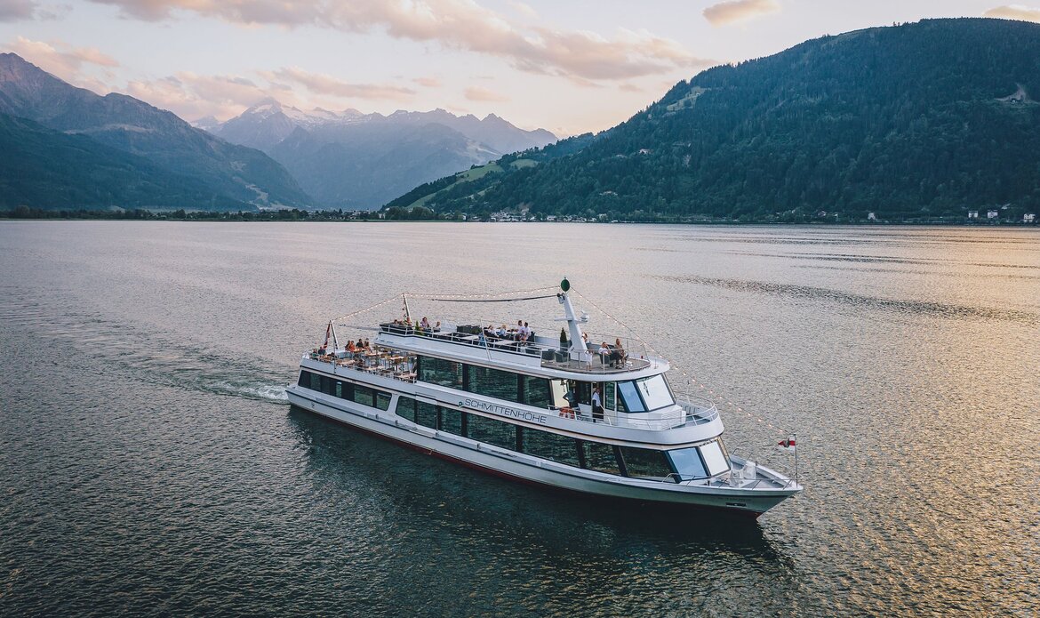 A passenger boat cruises across Lake Zell with mountains in the background at evening light.