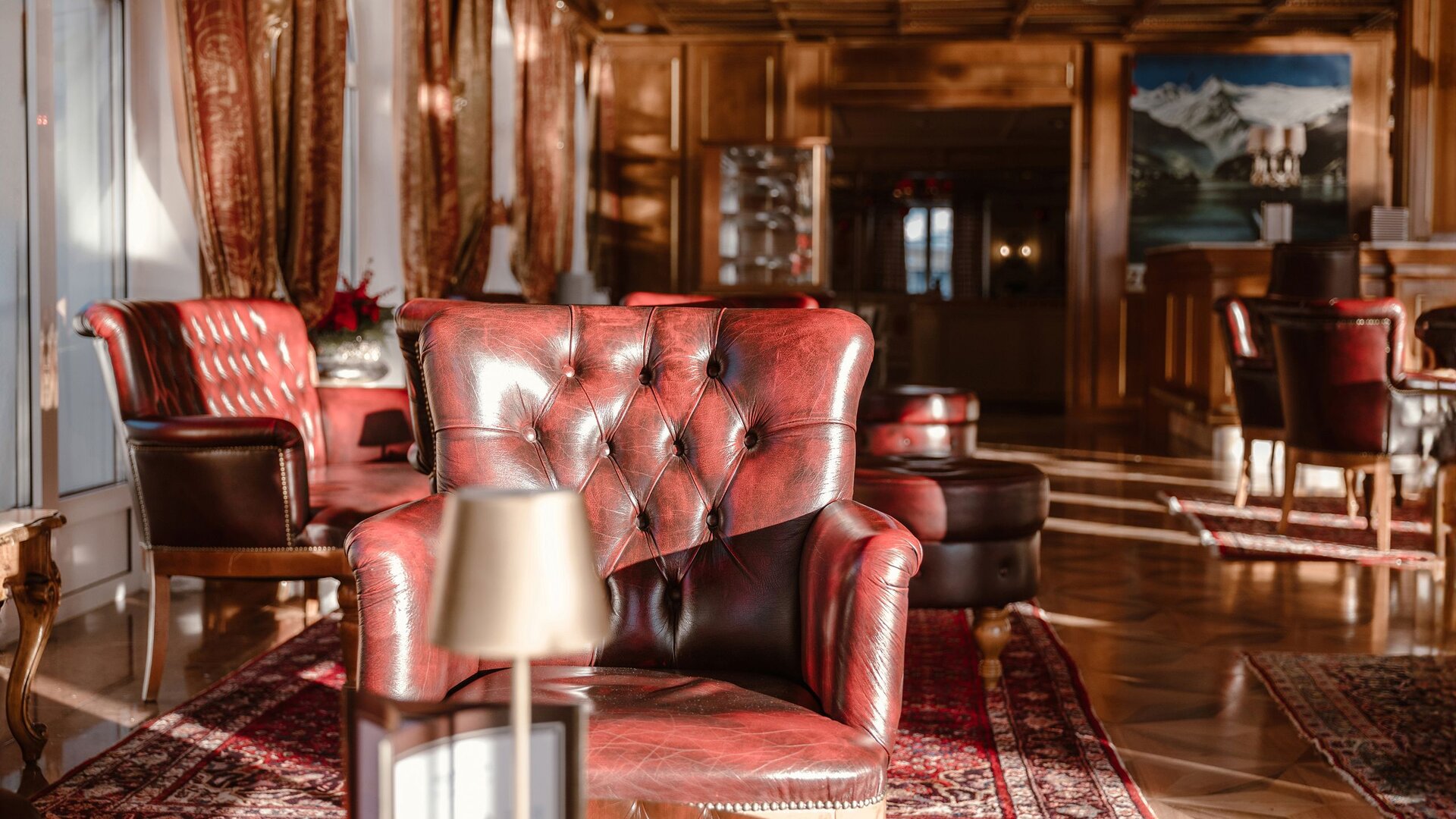 Rote Ledersessel und gemütliche Sitzgruppen in der Hotelbar mit Holzvertäfelung im GRAND HOTEL Zell am See.