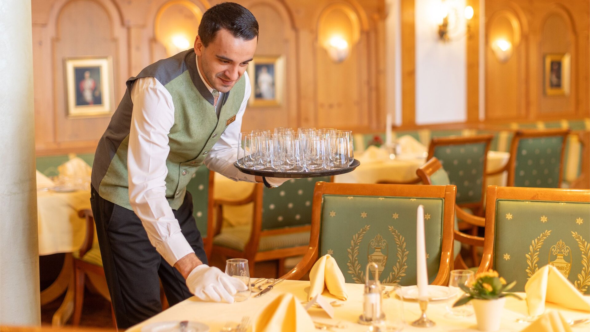 A waiter sets a table in the restaurant with glasses, candles, and white table settings.
