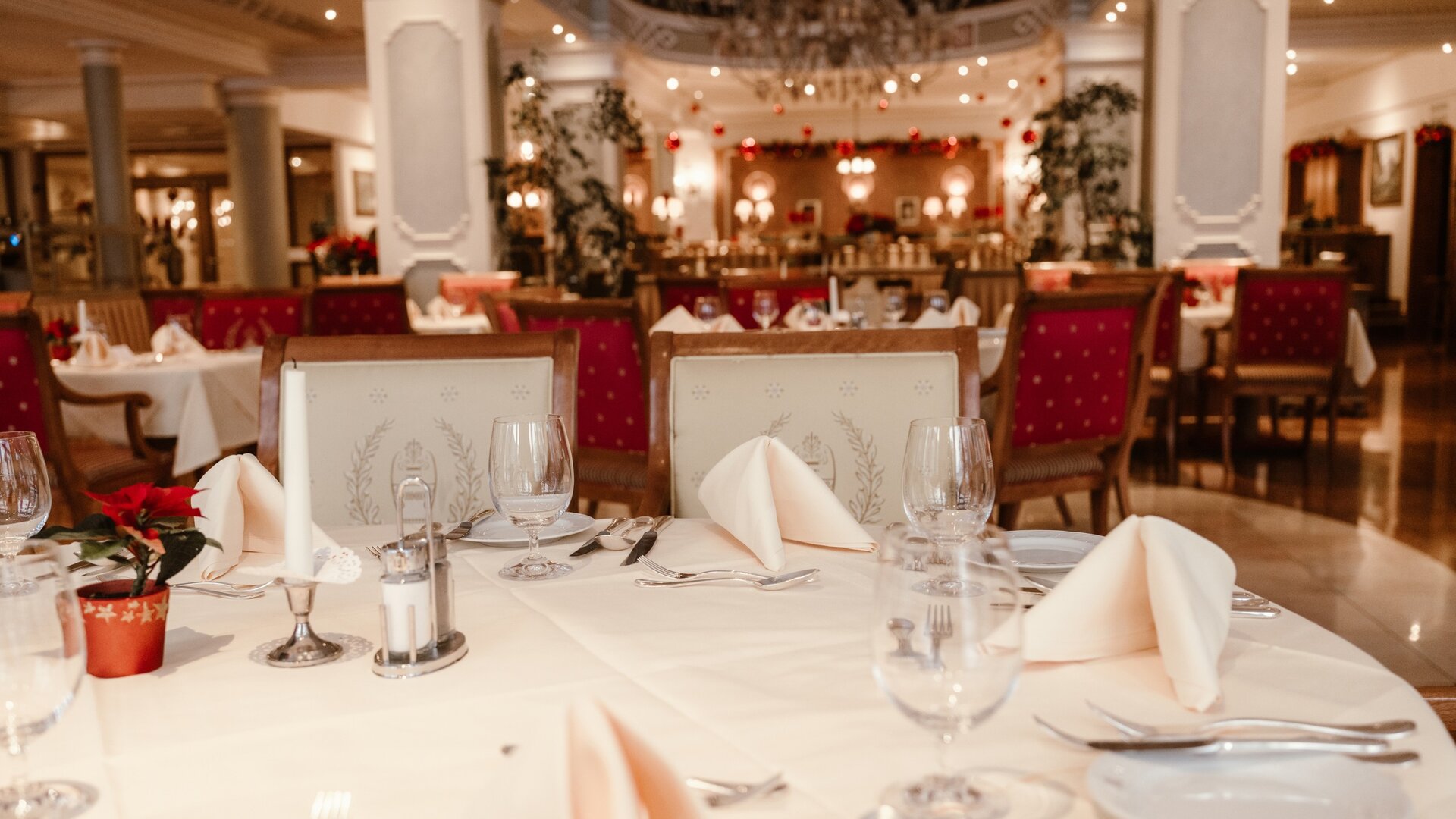 Ein elegant gedeckter Tisch im Hotelrestaurant mit gefalteten Servietten, Gläsern und roter Bestuhlung im Hintergrund.