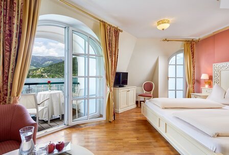 Hotelzimmer mit Balkon und Bergblick Ein helles Hotelzimmer mit Doppelbett, Balkon mit Tisch und Stuhl sowie Blick auf die Berge.