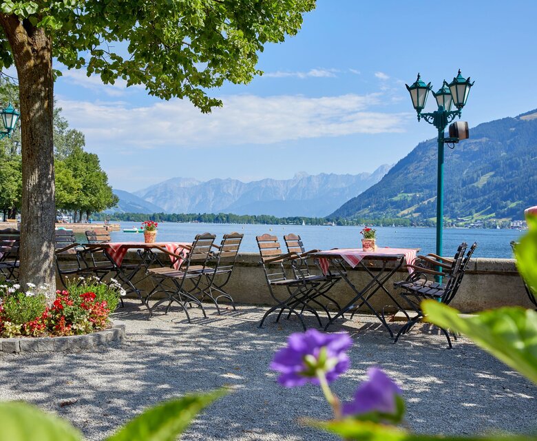 Tische und Stühle auf der Restaurantterrasse mit Blick auf den Zeller See und die Berge.