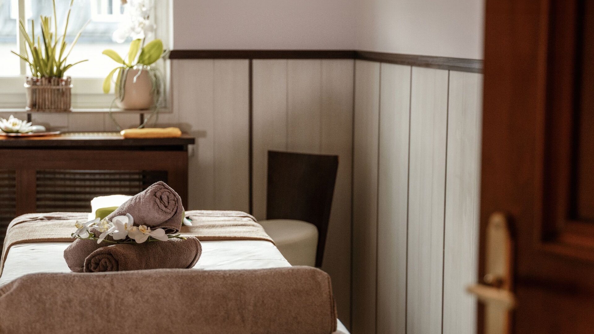 Ein Behandlungsbett mit aufgerollten Handtüchern steht in einem ruhigen Spa-Raum.
