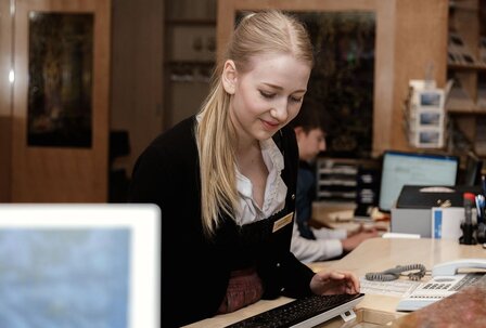 Karriere im Hotel: Rezeption im GRAND HOTEL Eine Mitarbeiterin arbeitet an der Hotelrezeption des GRAND HOTEL Zell am See und bedient den Computer.