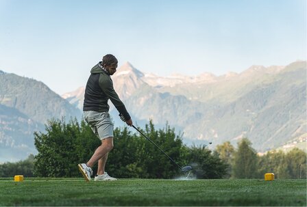 لاعب غولف يضرب الكرة في GRAND HOTEL Zell am See يلعب لاعب غولف ضربة البداية على ملعب غولف أمام خلفية جبلية.