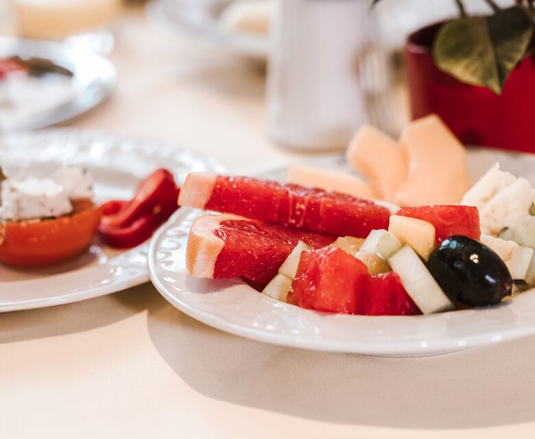 Ein Teller mit frischem Obst auf einem Buffet im Hotelrestaurant, im Hintergrund stehen weitere Speisen und ein Getränk.
