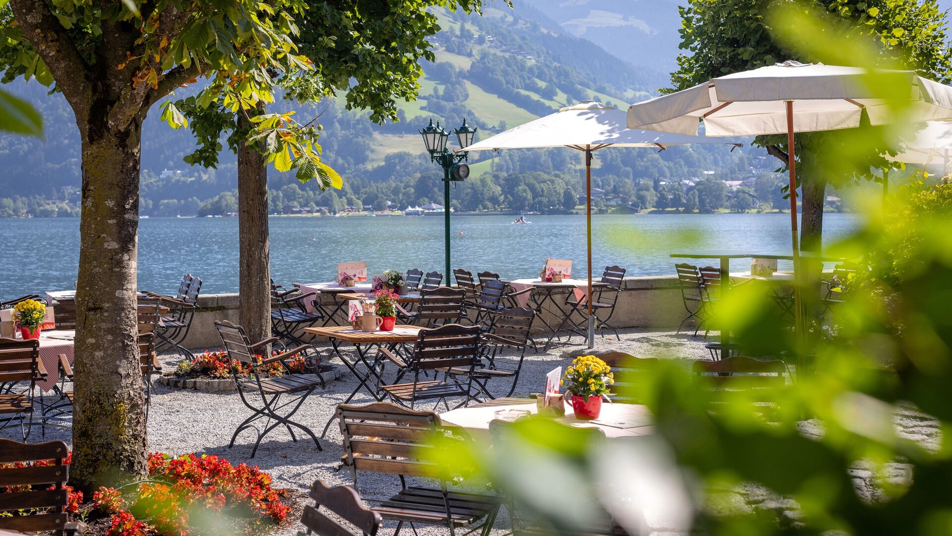 Ein Gastgarten mit Tischen, Stühlen und Sonnenschirmen liegt direkt am Zeller See.
