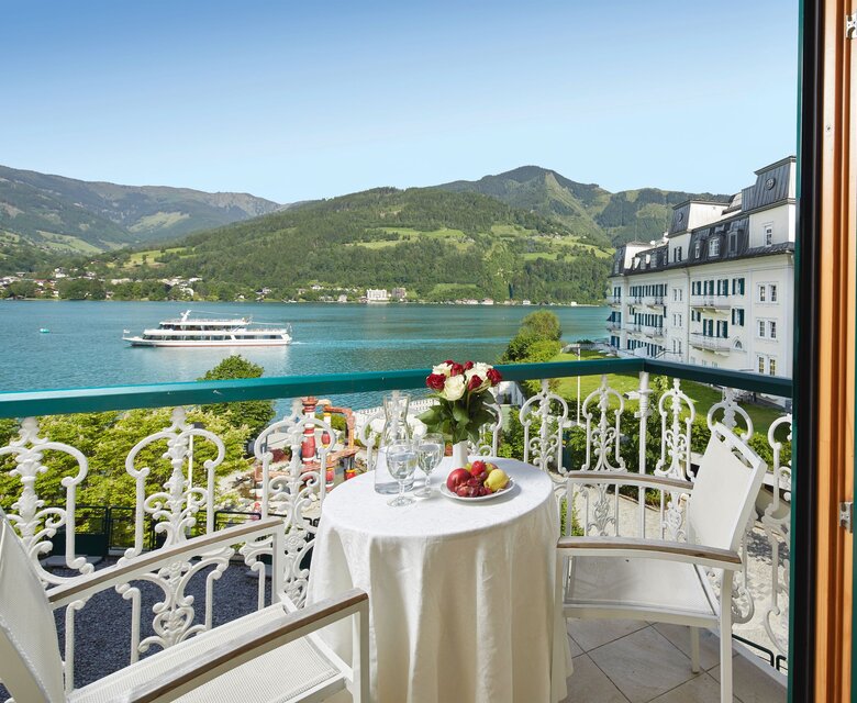 Ein Balkon mit Tisch, Stühlen und Blick auf den Zeller See sowie die Berge.