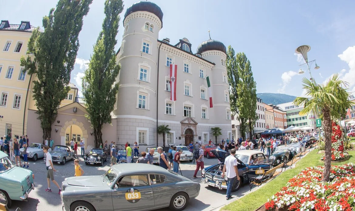 Mehrere Oldtimer stehen vor dem GRAND HOTEL Zell am See, während Menschen die Ausfahrt in der Stadt begleiten.