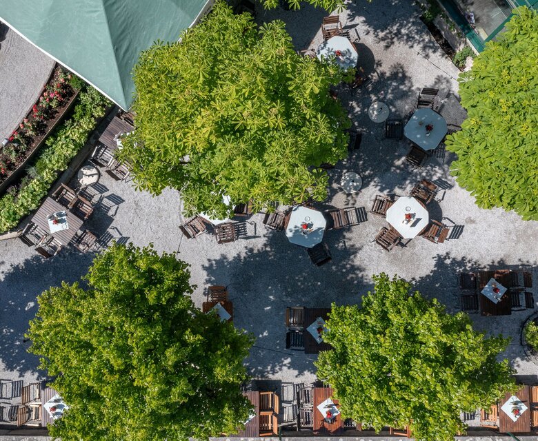 Blick von oben auf die Restaurantterrasse mit Tischen, Stühlen, Sonnenschirmen und Bäumen im GRAND HOTEL Zell am See.