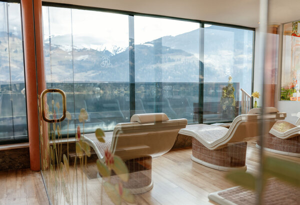 Leere Liegen im Ruheraum mit großen Panoramafenstern und Blick auf die Berge.