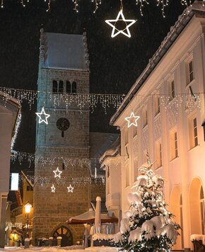 Ein beleuchteter Turm steht neben einem verschneiten Weihnachtsbaum und festlicher Lichterdekoration bei Nacht.
