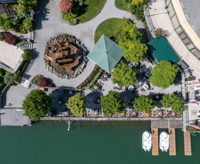 Luftaufnahme einer Restaurantterrasse am Wasser mit Sonnenschirmen, Liegen und Stegen im GRAND HOTEL Zell am See.