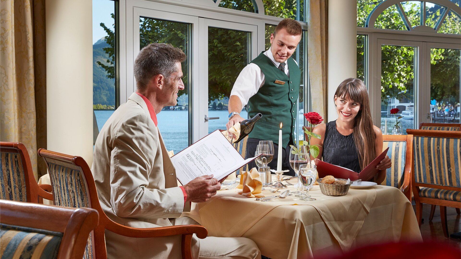 Ein Kellner serviert einem Paar im Hotelrestaurant am Zeller See die Speisekarte am gedeckten Tisch.