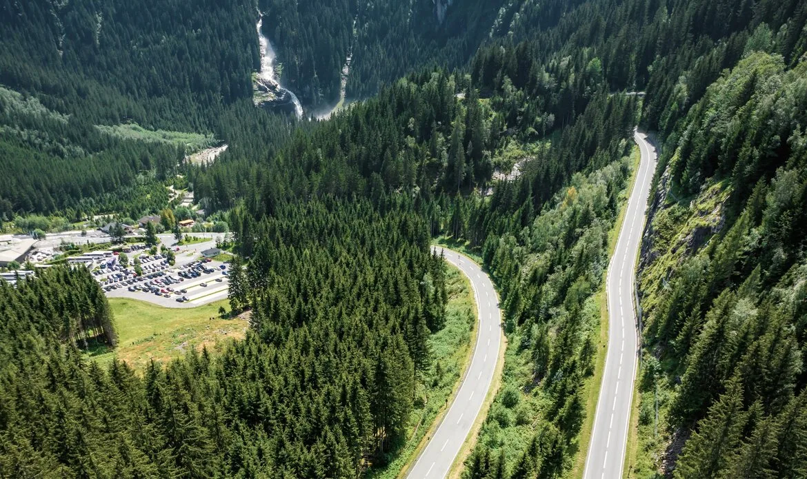 Eine kurvige Straße führt durch dicht bewaldete Berghänge oberhalb eines Tals im Salzburger Land.