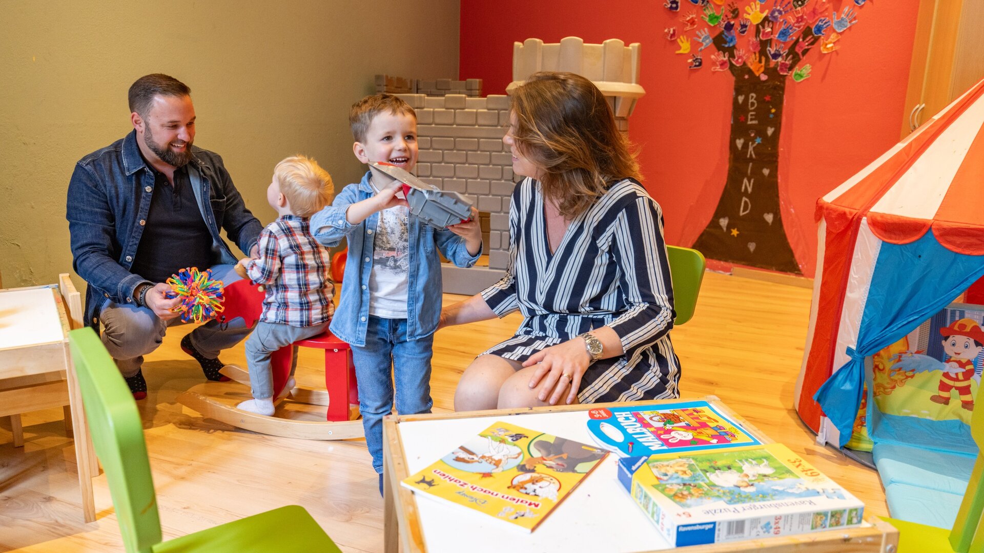 Ein Paar mit zwei kleinen Kindern sitzt im Familienbereich und spielt mit bunten Bausteinen.