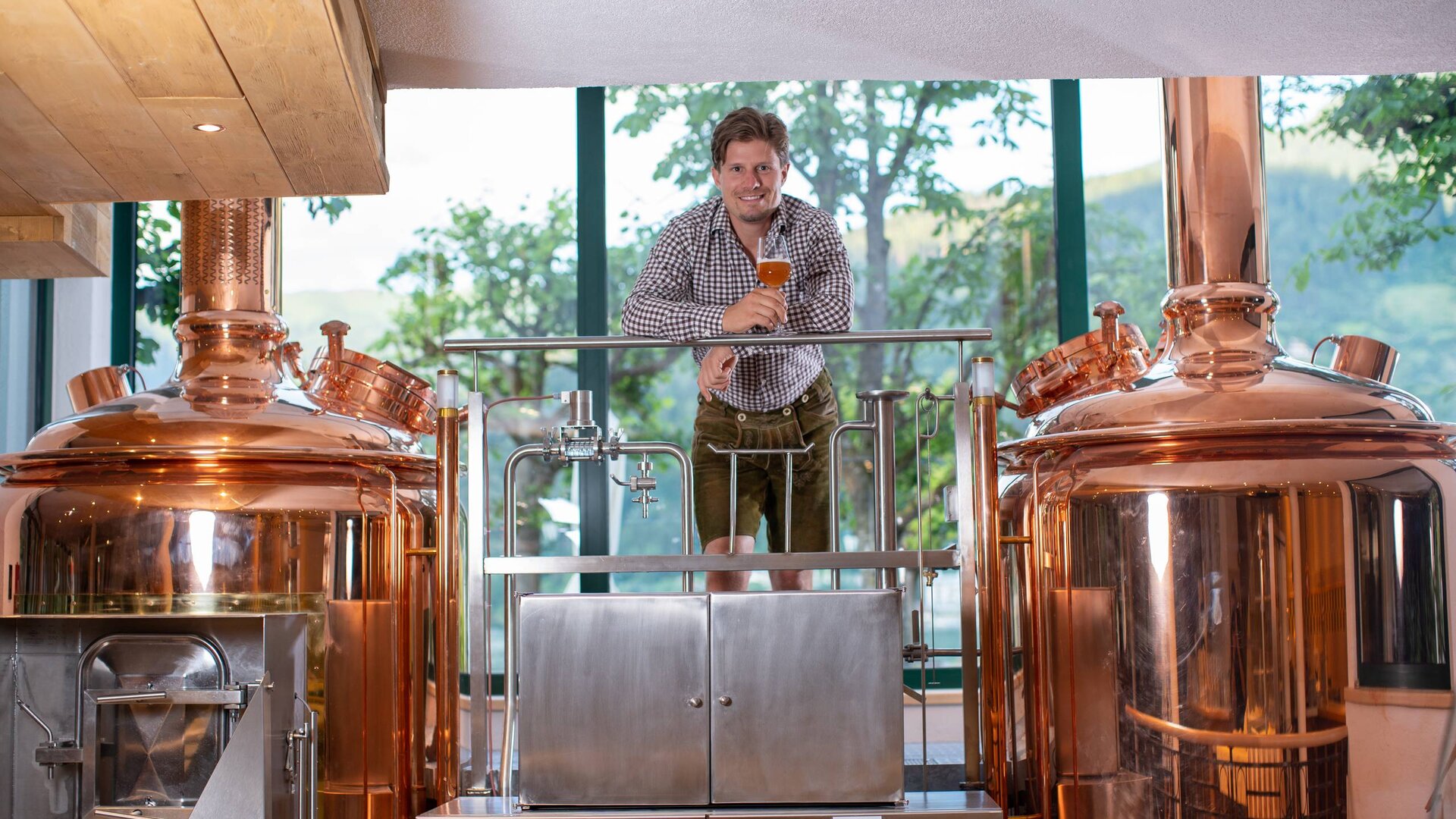Ein Mann steht zwischen kupfernen Braukesseln in der Hausbrauerei des Pinzga Bräu.