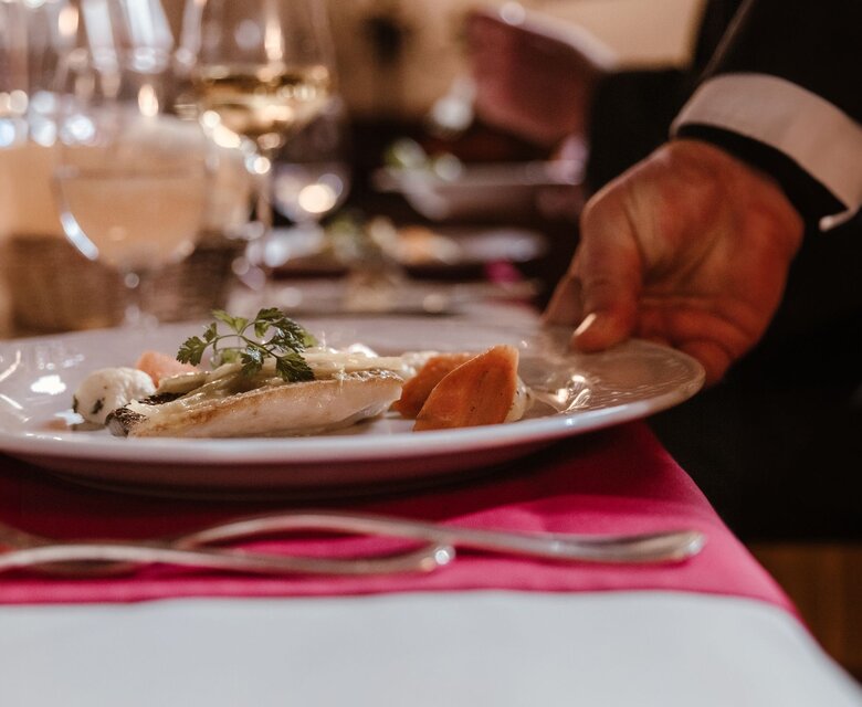 Ein Kellner serviert in einem Hotelrestaurant einen Teller mit Fischgericht am gedeckten Tisch.